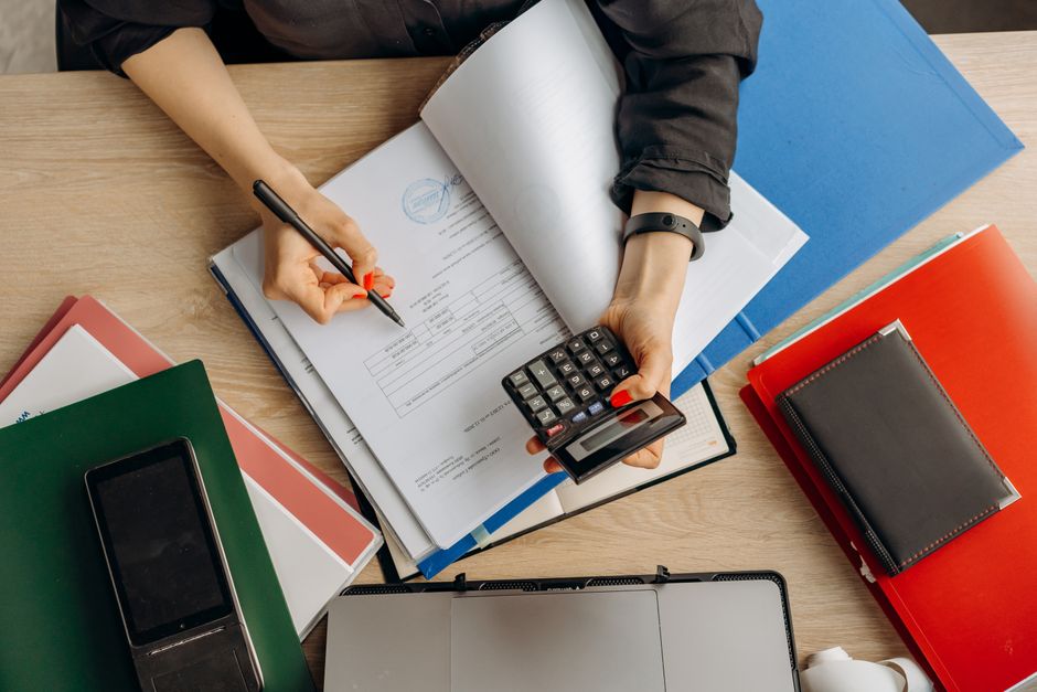 Persona usando una calculadora sobre documentos de costos y contabilidad