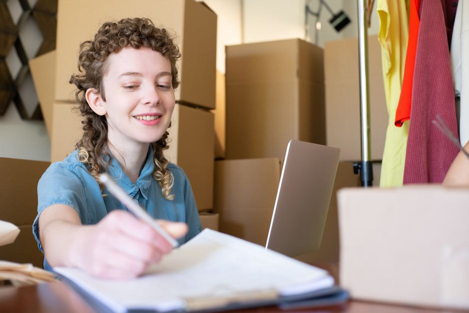 Emprendedora anotando datos de envío de sus pedidos entre cajas listas para despachar